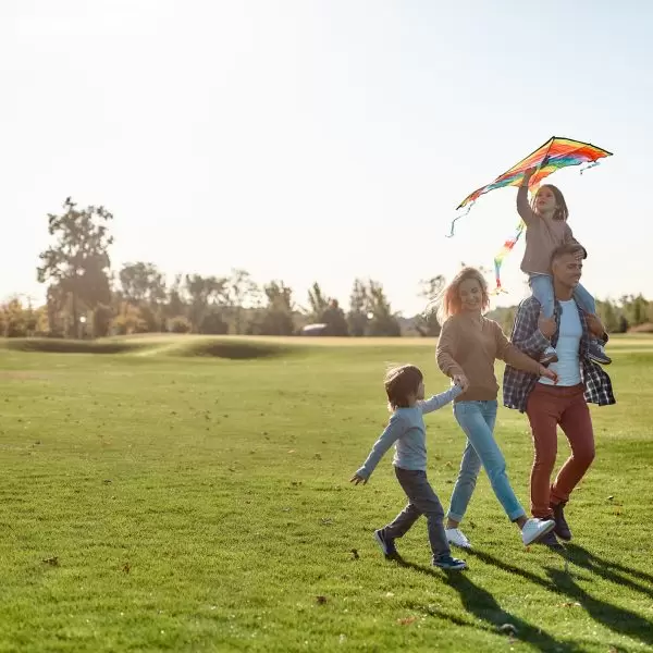 Full-length portrait of cheerful parents with two kids running with kite in the park on a sunny day. Family, kids and nature concept. Horizontal shot.