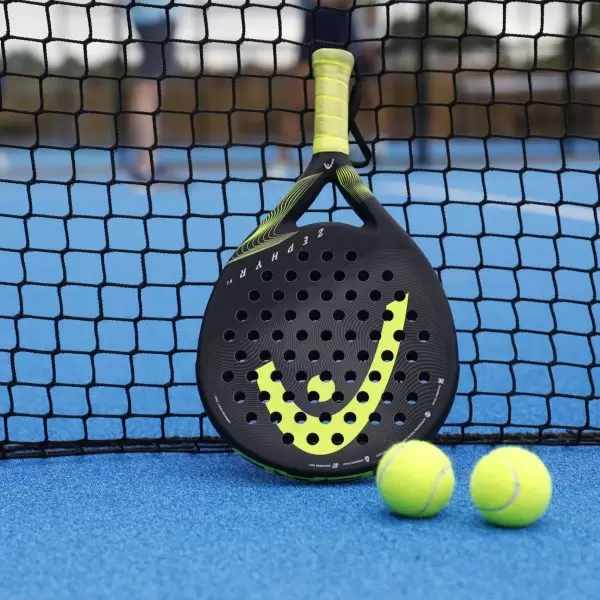 A paddle racket and two tennis balls rest against the net at the Minthis Paddle court