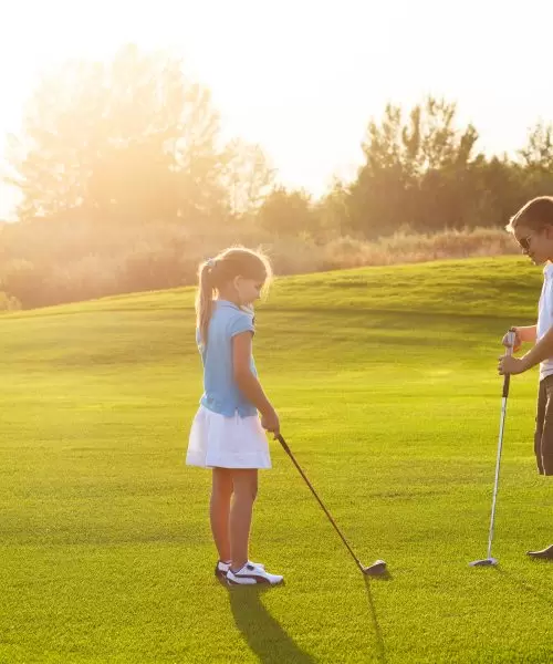 Casual kids at a golf field holding golf clubs. Sunset