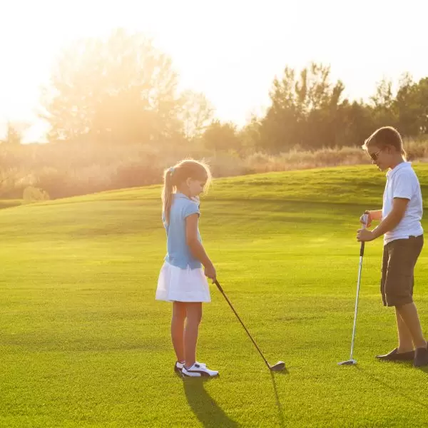 Casual kids at a golf field holding golf clubs. Sunset